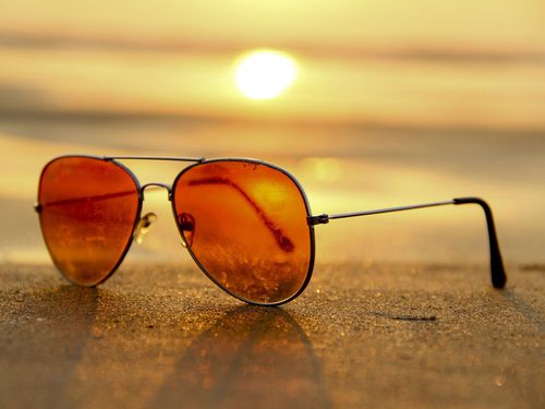 Sonnenbrille steht auf Sand mit Meer und Sonnenuntergang im Hintergrund